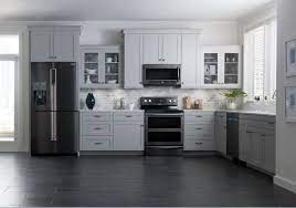 White kitchen with stacked wall cabinets, custom range hood, and large island with plenty of seating. Is Black The New Stainless Steel Black Appliances Kitchen Kitchen Design Home Kitchens