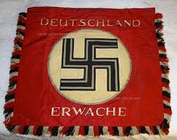 The flag background is red silk with white ribbed silk circle in the middle with a black silk swastika with the front top of the flag says deutschland erwache. Deutschland Erwache Standard Flag