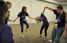 Use varying sizes of hula hoops to adjust to your group size or to make it more challenging. Students Race To Pass A Hula Hoop Around Each Other While Holding Hands As They Play Cooperative Games While Pa Youth Games Cooperative Games Youth Group Games