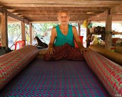 An artisan woman weaving a colorful rug on a traditional wooden loom in Cambodia