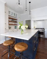 Glass orb pendants above a navy blue kitchen island completed with a glass front beverage fridge, a white quartz countertop, and a stunning centerpiece. Navy White Kitchen Karen Kettler Design