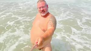 O velho homem de cabelos grisalhos gordo tem dia nu e cums na praia