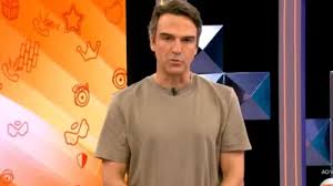 Tadeu Schmidt, apresentador do Big Brother Brasil, em estúdio com fundo temático do programa.