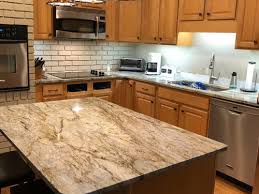 White kitchen shelves with metal chains hang in front of a white brick tile backsplash beneath a white plank ceiling and over white cabinets contrasted with a black quartz countertop. Ideas For Backsplash Next To Existing Painted Brick Wall