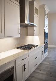White quartz counters with stainless steel hood and brass pendant light fixtures. All White Custom Kitchen With Stainless Steel Appliances White Shaker Kitchen White Shaker Kitchen Cabinets Greige Kitchen Cabinets