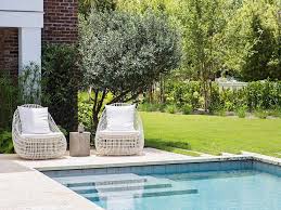 On Either Side Of A Round Concrete Accent Table White Pod Chairs Sit At A Rectangular In Ground Swimming Pool Outdoor Pool Area Outdoor Backyard Pool