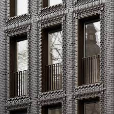 The tiered, 'wedding cake' form of the building, while also providing interest in form also played homage to this role as a gateway building. Bureau De Change Inserts Textured Black Brick Building Into London Terrace
