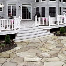 The rich, warm tones of the stone used in the patio go well with the neutral brown clapboard façade of the house, and also goes well with neutral blue color used in the patio furniture. Flagstone Paver Patio Leads To Low Maintenance Deck Archadeck Outdoor Living