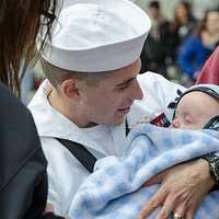 Cmdr. Dave Stoner holds his granddaughter for the first time during the  ship's return to Naval Station Norfolk.