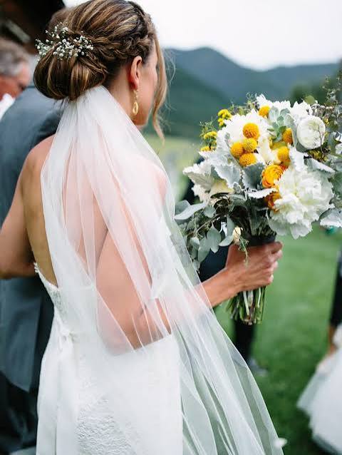 Tuck the veil under a chic, braided bun and accent with small flowers for an effortless-looking wedding day hairstyle.