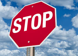 Image: bright red stop sign against a blue sky with white puffy clouds