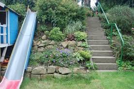 Eine kleine spielfläche ist mit schaukeln und rutschbahn ausgestattet. Rutsche Am Hang Gartenwildwuchs Sloped Garden Slope Garden Sloped Backyard