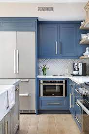 Lovely blue kitchen features a blue island accented with a black countertops, while blue cabinets donning vintage cup pulls flank a stainless steel range positioned beneath a blue range hood. A Stainless Steel Refrigerator Is Recessed Beside Blue Shaker Cabinets Adorned With Brass Pulls And Fixe Kitchen Renovation New Kitchen Cabinets Kitchen Design