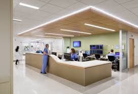 A Man In Blue Scrubs Speaks To A Woman In Blue Scrubs Behind A Desk Hospital Interior Hospital Interior Design Healthcare Interior Design