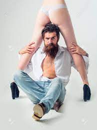 Handsome Bearded Man With Long Beard And Moustache On Serious Face Sitting  Near Sexy Female Legs And Buttocks In Lingerie And Shoes Of Young Pretty  Girl In Studio Isolated On White Background