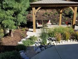 A Residential Rear Yard With Low Water Plantings Rocks And A Concrete Seating Area Desertl Mediterranean Landscaping Low Water Landscaping Desert Landscaping