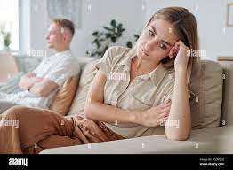 Young upset and lonely wife sitting on couch while expressing offense to  husband Stock Photo - Alamy