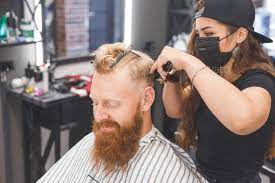 Woman barber making haircut to redhaired man with beard in barbershop Stock Photo by Vladdeep