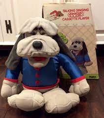 yipper, a gray and orange furred puppy, has just been placed in a kennel. yipper: Rare 1986 Pound Puppies Cooler Animated Plush Iob By Tonka Singing Pound Puppy Talking Pound Puppy Animated Dogs Coo Pound Puppies Animated Plush Puppies