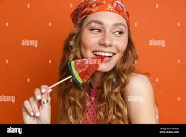 Young ginger woman wearing bandana smiling while licking lollipop isolated  over orange wall Stock Photo - Alamy