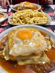La francesinha est une sandwich créée dans la ville de porto, fait avec deux tranches de pain légèrement grillées, parmi lesquels est ajouté un steak de vache, saucisse fumé, mortadelle. Francesinha Portuguese Sandwich Made With Bread Ham Fresh Sausage And Covered With Melted Cheese And A Hot Thick Tomato And Beer Sauce Served With French Fries Eatsandwiches