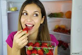 Vicino di bella ragazza sorridente vicino al frigo mangiare fragola - foto  d'archivio | Crushpixel