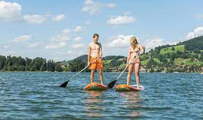 Junger Mann und junge Frau auf einem Stehpaddel Board, Stand-Up-Paddel oder SUP  auf einem See, Schli