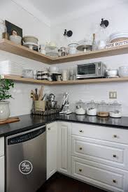 White and black kitchen features glass upper cabinets and black lower cabinets paired with white quartz countertops and a white beveled subway tile a modern mobile chandelier illuminates a large black center island topped with black countertops fitted with a stainless steel sink and modern. Joining The Open Shelf Posse In The Kitchen Oliver And Rust Vintage Interiors In 2021 Black Kitchen Countertops White Cabinets Black Countertops Black Countertops