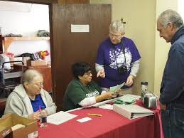 Left to right behind the table: Sr. Lawdean Lamberger, Sr.…