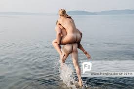 Nackter Mann gibt nackte Frau huckepack ins Wasser