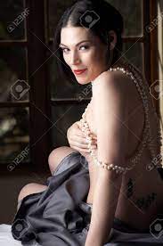 セクシーな若い白人アダルトで裸の女性赤い唇、短い黒い髪、黒いサテンのシートとベッドの上に座っていると身に着けている真珠の文字列で覆われて、ピアス眉の写真素材・画像素材  Image 8239534