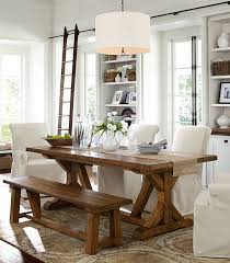 The bright dining room boasts a jute rug and black lantern pendant that hung over the wooden dining table surrounded by beige wingback chairs, a cushioned bench, and tufted ottomans. Pin On House Ideas