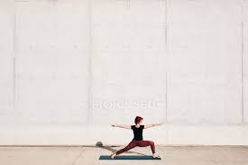 Great pose for athletes and dancers. Side View Of Trendy Fit Female Athlete In Sportswear Doing Warrior Two Yoga Pose On Sports Mat While Training Alone On Street Gymnastic Person Stock Photo 357488250