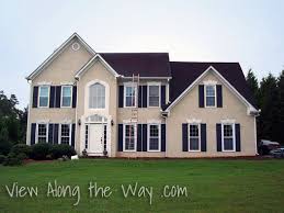 The entrance and garage with space for three cars. House Exterior Beige With Black Shutters And Black Roof Tan House Black House Exterior House Exterior