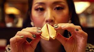 Woman holding and examining fortune cookie in a restaurant setting