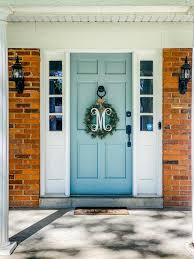 A black front door with brass hardware is surrounded by glass insets and white trims designed with intricate details making it stand out against the brick. How To Pick The Perfect Color Paint For Your Front Door Emmy Lou Styles