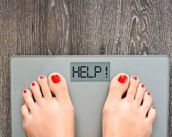 person smiling and holding up a scale that shows they have lost weight