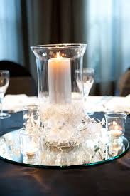 Add some reflection to your wedding centerpieces! Glass Hurricane On A Round Mirror With Wreath Garland Stunning Hurricane Glass Centerpiece Round Wedding Reception Tables Round Table Centerpieces