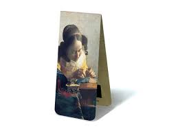 The work shows a young woman dressed in a yellow shawl, holding up a pair of bobbins in her left hand as she carefully places a pin in the pillow on which she is making her bobbin lace. Magnetic Bookmark The Lacemaker J Vermeer Museum Webshop Museum Webshop