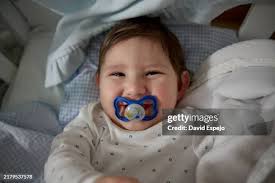 Smiling Baby Boy Lying In Crib With Pacifier High-Res Stock Photo