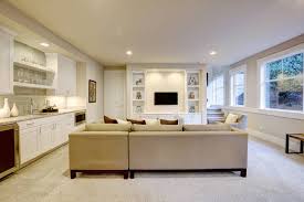 Contemporary basement tv room features a brown leather sofa with brass nailhead trim flanked by seagrass end tables alongside a pair of beige tufted slipper chairs, facing. 62 Finished Basement Ideas Photos