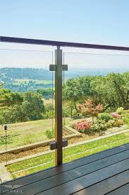 The serene beauty of this mountain lake shines through stained wood decking and railing is combined with stock metal balusters and a continuous wood top rail in this comfortable outdoor living space. Glass Railing For A Scenic Deck Railings Outdoor Glass Railing Glass Railing Deck