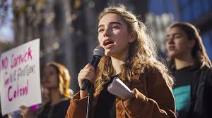 A youth advocate speaking into a microphone at a community hearing.
