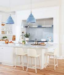 How many times have you heard 'home is where the heart is'? White Kitchen Blue Pendant Lights Marble Countertop Barstools Open Shelving Andrew Howard Interior Design Katie Considers