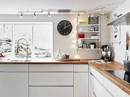 Una cocina con muebles blancos y objetos de decoración o algún mueble de madera parece los tallos verdes refrescar el interior blanco al igual que la madera. Cocina En Blanco Madera Y Acero