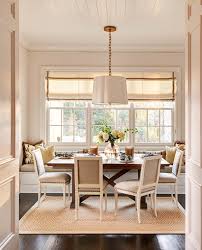 Trestle dining table with black bamboo chairs in a dining room surrounded with stunning warm wood floors. Banquette Window Seat Transitional Dining Room Carolina Design Associates