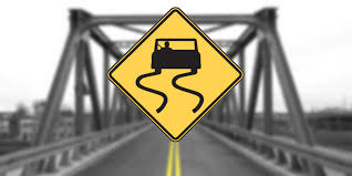 Yellow with black symbol of a skidding car posted: What Does The Slippery When Wet Sign Mean