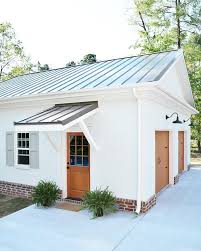 Black And White House With Wood Garage Door White Transitional Farmhouse Garage With Metal Roof Wood Garage Doors Shutters And Brick Foundation Detail Farmhouse Garage House Exterior Wood Garage Doors