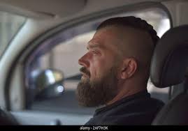 Ein junger Mann mit einem Bart reitet auf dem Rücksitz des Autos. Ein Mann  mit einem Bart Fahrten im Auto auf dem Beifahrersitz Stockfotografie