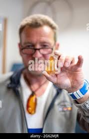 Kloster, Germany. 26th June, 2021. Henry Engels (53) holds an amber in the  sun. The native of Hiddensee has been running an amber workshop for 20  years. He makes earrings, necklaces and
